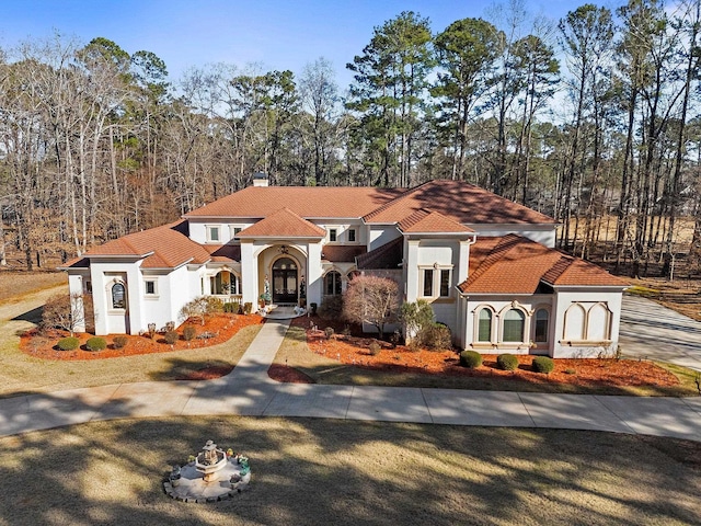 mediterranean / spanish-style house featuring stucco siding, a chimney, and a tiled roof