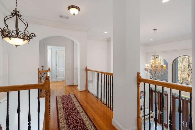 hallway featuring wood finished floors, visible vents, an inviting chandelier, ornamental molding, and an upstairs landing