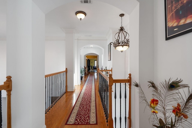 corridor featuring arched walkways, an upstairs landing, light wood-style floors, and ornamental molding