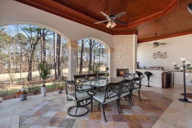 view of patio / terrace featuring ceiling fan, outdoor dining area, an outdoor stone fireplace, and an outdoor kitchen