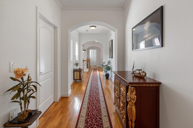 hall featuring crown molding, light wood-style floors, arched walkways, and baseboards