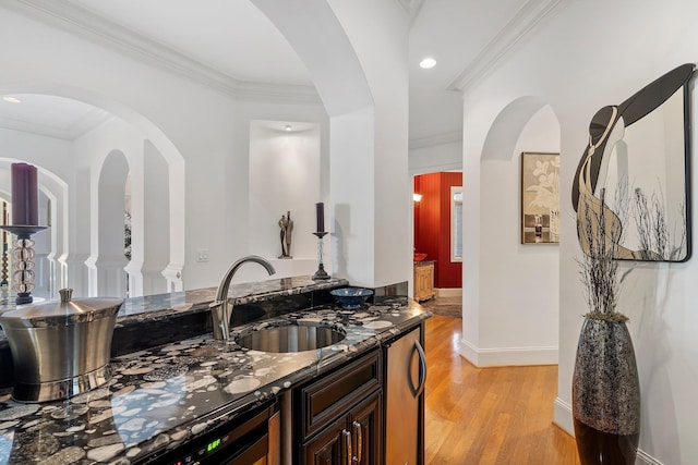 kitchen featuring crown molding, baseboards, light wood-type flooring, dark stone countertops, and a sink