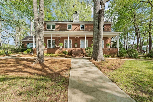 view of front of property featuring covered porch, a chimney, ceiling fan, and brick siding