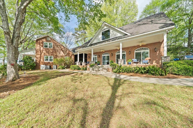view of front of house with a ceiling fan, covered porch, brick siding, and a front yard