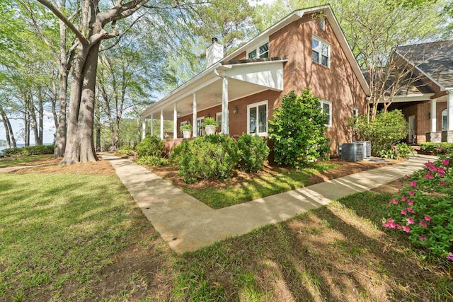 view of home's exterior with a lawn, central AC unit, a chimney, and brick siding