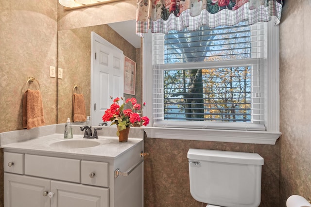 half bath with vanity, a healthy amount of sunlight, and toilet
