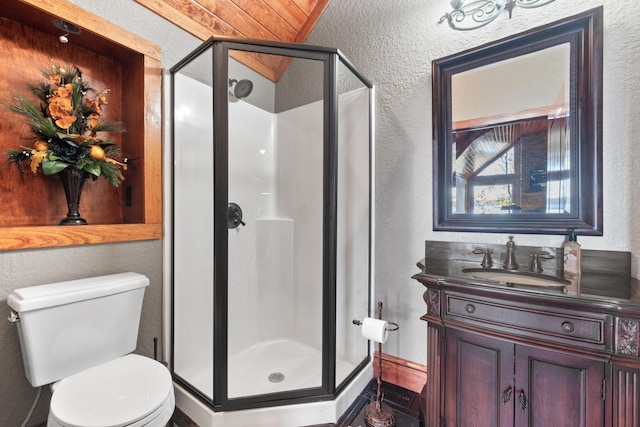 full bath with vanity, a textured wall, a stall shower, and toilet