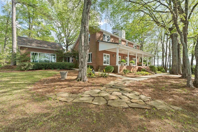 rear view of house featuring a chimney, a porch, and brick siding