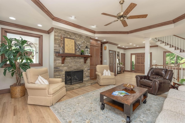 living room with a raised ceiling, crown molding, a stone fireplace, and light wood-type flooring