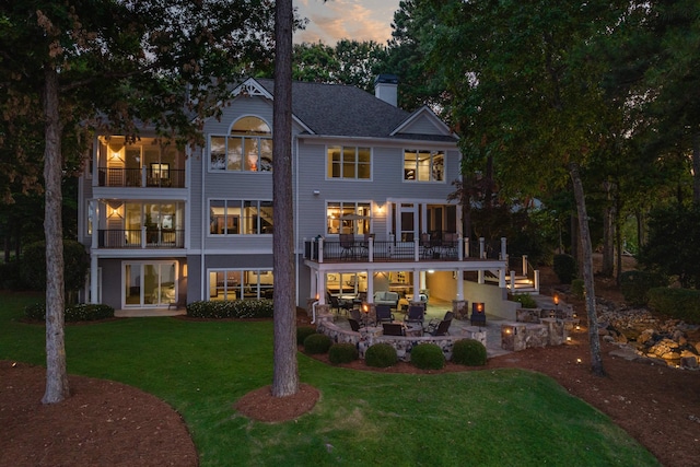 back house at dusk with a balcony, a lawn, and a patio area