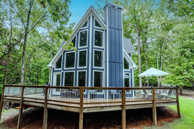 rear view of property featuring board and batten siding, roof with shingles, a deck with water view, and a chimney