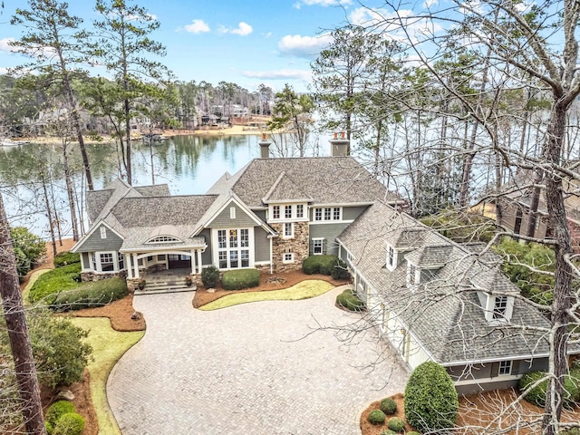 view of front facade featuring a water view, a chimney, driveway, and a shingled roof