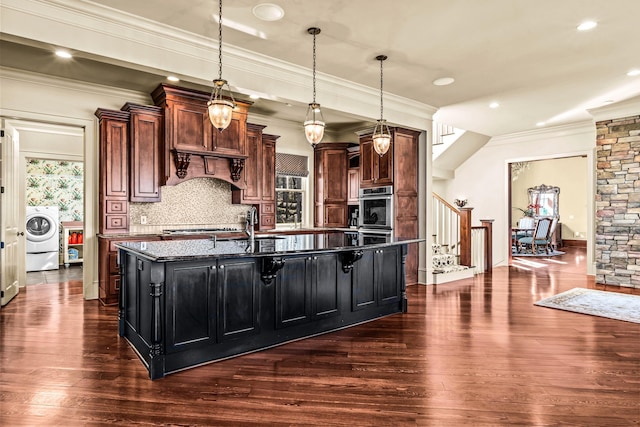 kitchen featuring a kitchen island with sink, backsplash, ornamental molding, washer / clothes dryer, and dark wood-style flooring