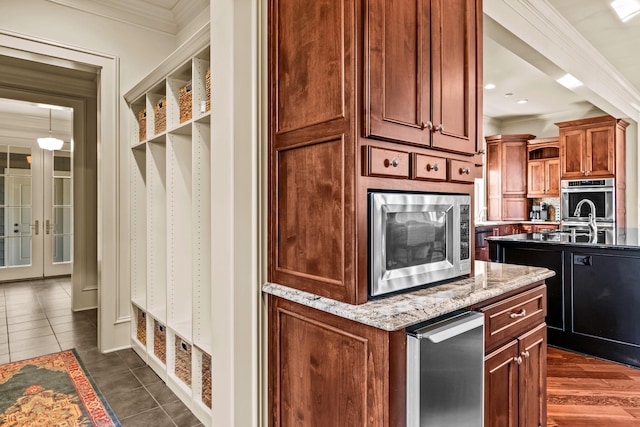 kitchen featuring crown molding, dark tile patterned floors, light stone counters, stainless steel appliances, and a kitchen island with sink