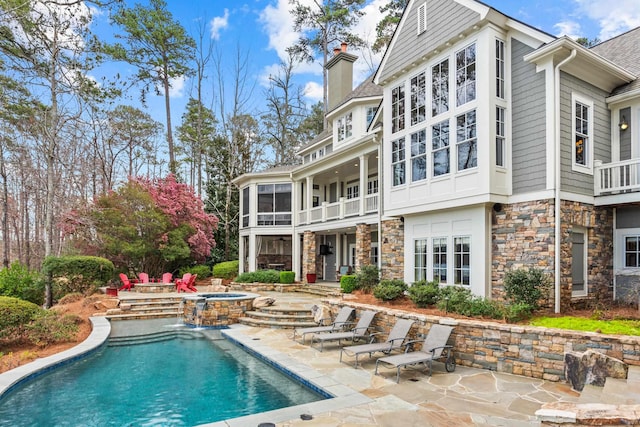 rear view of property featuring a patio area, stone siding, and a chimney