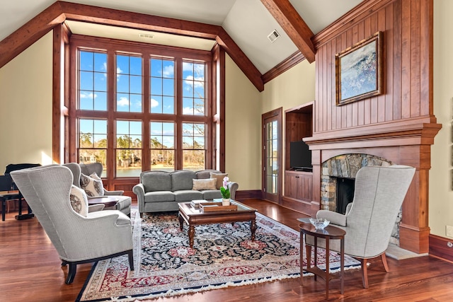 living room with beam ceiling, a stone fireplace, baseboards, and wood finished floors