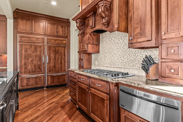 kitchen featuring light stone counters, backsplash, dark wood finished floors, stainless steel gas stovetop, and paneled built in refrigerator