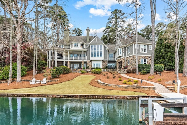 rear view of property featuring a water view, a chimney, a yard, a balcony, and stone siding