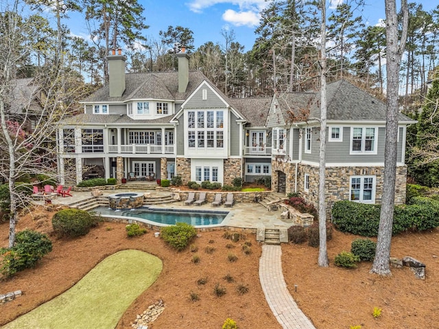 back of house with stairs, a chimney, a balcony, stone siding, and a patio