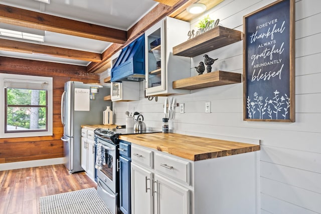 kitchen featuring stainless steel appliances, white cabinetry, butcher block countertops, and wood walls