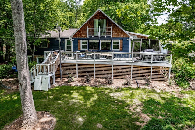 rear view of house featuring a wooden deck, a sunroom, and a lawn