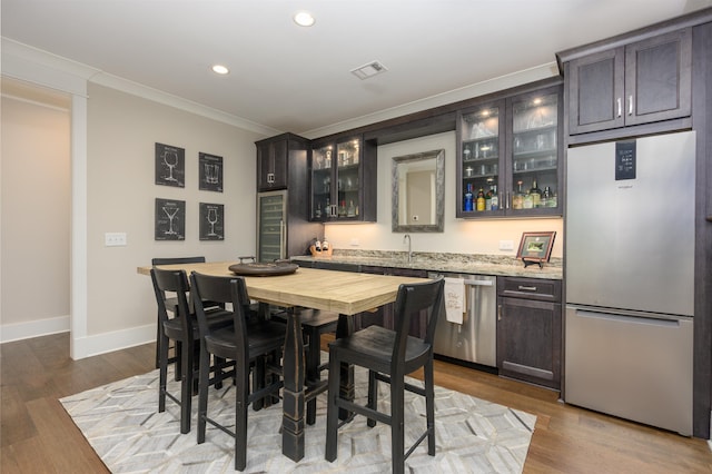 dining space featuring bar with sink, ornamental molding, recessed lighting, beverage cooler, and dark wood-type flooring