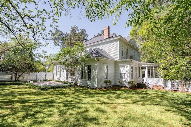 rear view of house featuring a lawn, a sunroom, and a patio