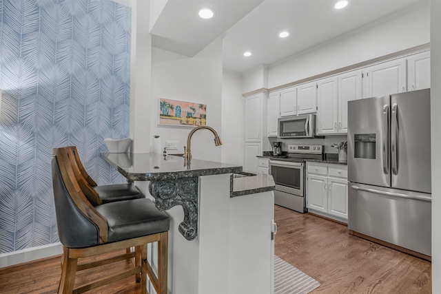 kitchen featuring stainless steel appliances, light hardwood / wood-style flooring, white cabinets, and kitchen peninsula