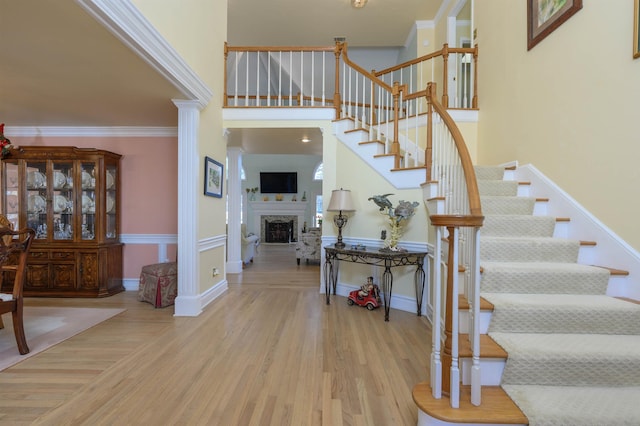 stairs featuring decorative columns, wood-type flooring, a towering ceiling, and crown molding