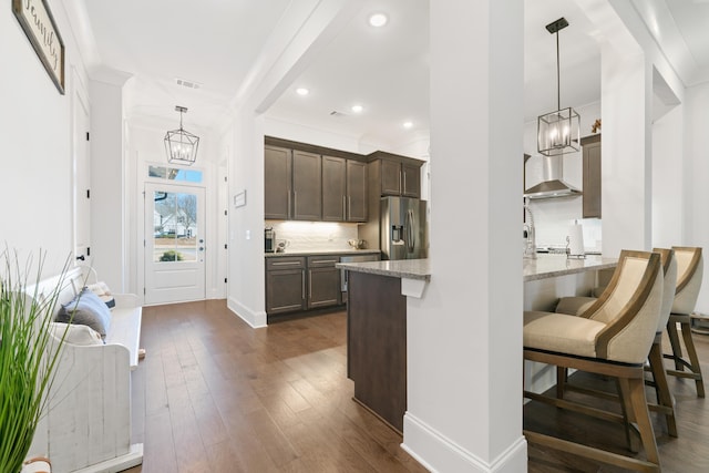 kitchen featuring a kitchen breakfast bar, hanging light fixtures, stainless steel fridge with ice dispenser, light stone countertops, and dark brown cabinets