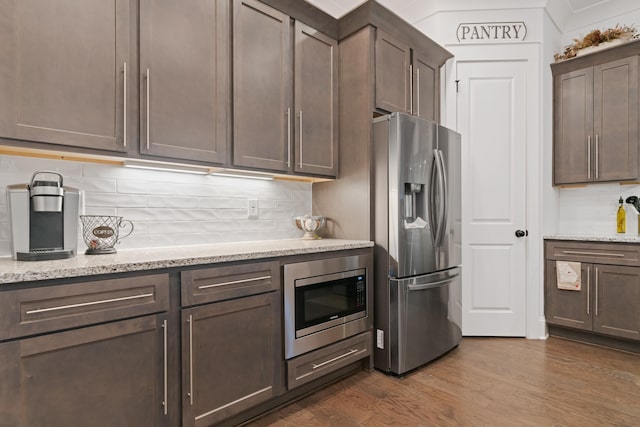 kitchen with dark wood-type flooring, stainless steel appliances, tasteful backsplash, dark brown cabinetry, and light stone countertops