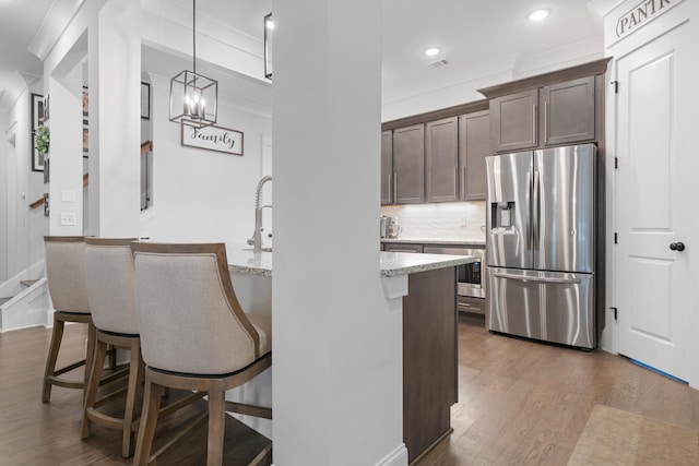 kitchen with stainless steel fridge, dark wood-type flooring, a breakfast bar, dark brown cabinets, and light stone counters