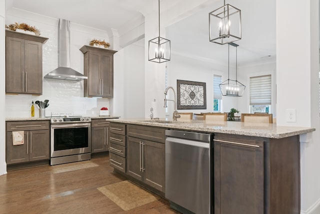 kitchen with sink, stainless steel appliances, hanging light fixtures, and wall chimney exhaust hood