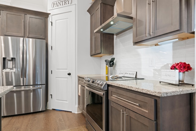 kitchen featuring hardwood / wood-style flooring, stainless steel appliances, tasteful backsplash, light stone countertops, and wall chimney exhaust hood