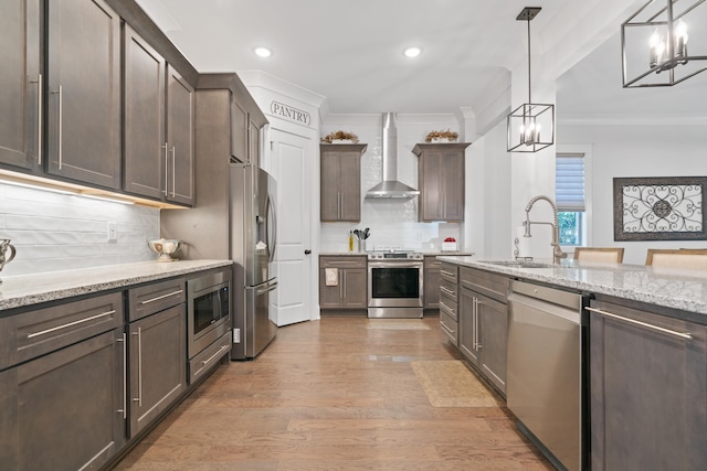 kitchen with wall chimney exhaust hood, sink, decorative light fixtures, stainless steel appliances, and light stone countertops