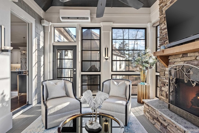 sitting room featuring a stone fireplace, vaulted ceiling, and a wall unit AC