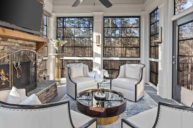 sunroom featuring plenty of natural light, a stone fireplace, and ceiling fan