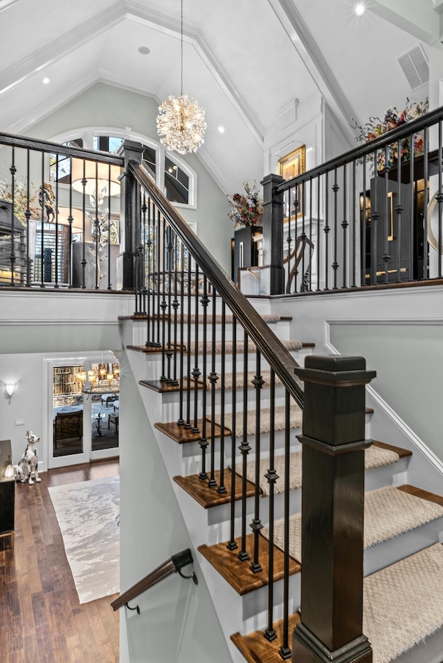 stairs with hardwood / wood-style flooring, high vaulted ceiling, and a notable chandelier