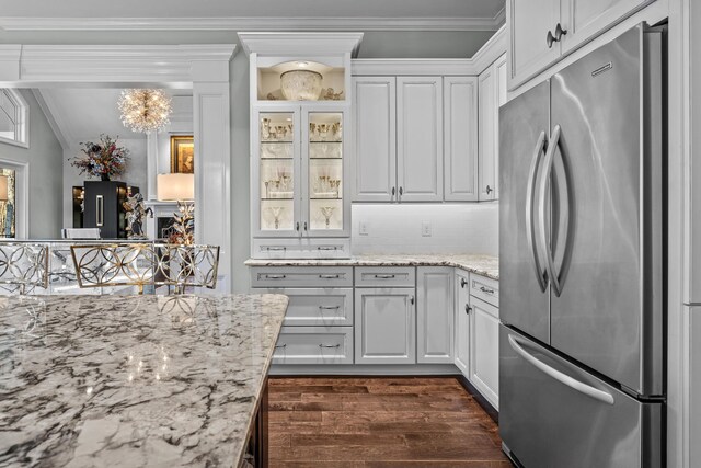 kitchen featuring light stone counters, ornamental molding, stainless steel refrigerator, and white cabinets