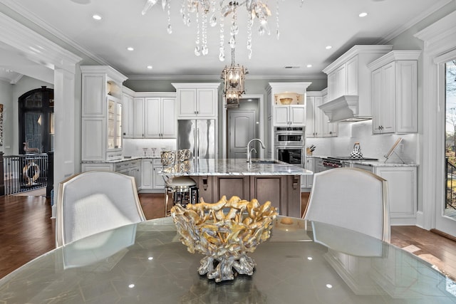 kitchen featuring hanging light fixtures, stainless steel appliances, a kitchen breakfast bar, light stone countertops, and an island with sink