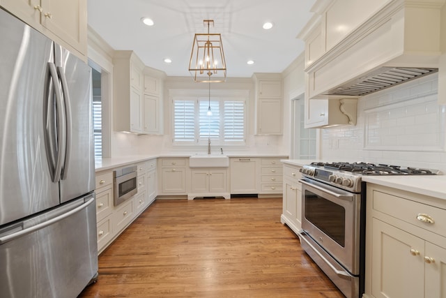 kitchen with premium range hood, sink, light wood-type flooring, appliances with stainless steel finishes, and pendant lighting