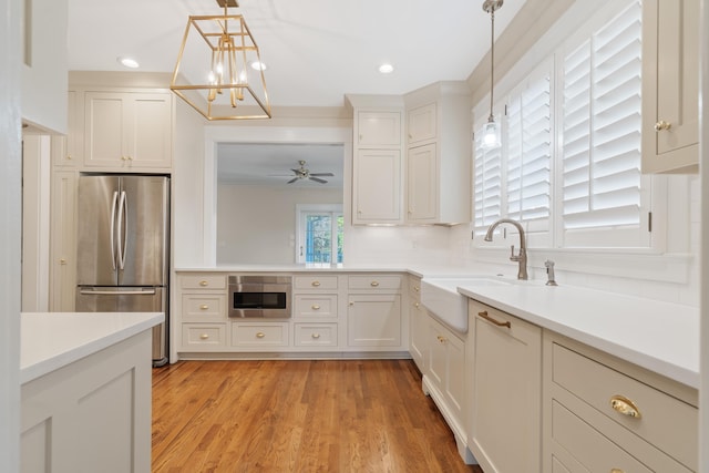 kitchen with white cabinetry, sink, stainless steel refrigerator, and decorative light fixtures