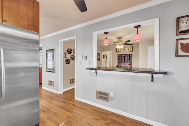 kitchen featuring stainless steel fridge, ornamental molding, decorative light fixtures, kitchen peninsula, and light wood-type flooring