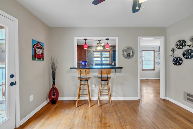 kitchen with ceiling fan, wood-type flooring, kitchen peninsula, and a breakfast bar area