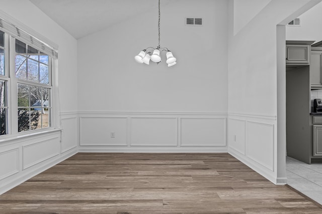 unfurnished dining area featuring vaulted ceiling, wood finished floors, visible vents, and a notable chandelier