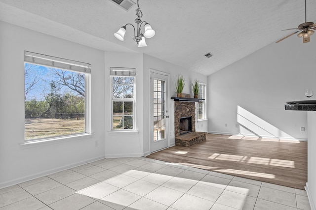 unfurnished living room with ceiling fan with notable chandelier, a fireplace, visible vents, vaulted ceiling, and tile patterned floors