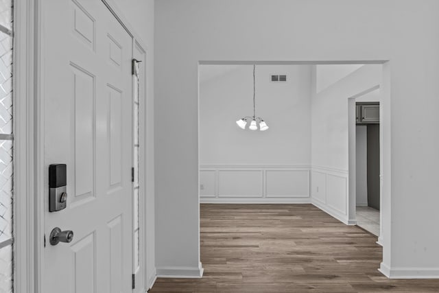 foyer featuring a chandelier, a decorative wall, a wainscoted wall, wood finished floors, and visible vents