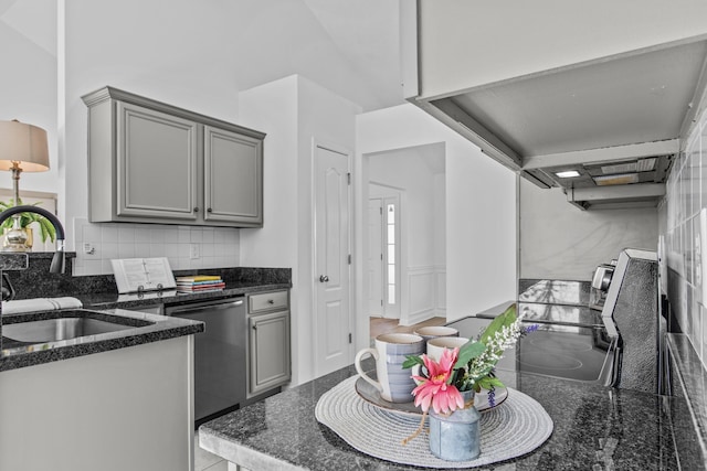 kitchen featuring stainless steel dishwasher, backsplash, a sink, and gray cabinetry