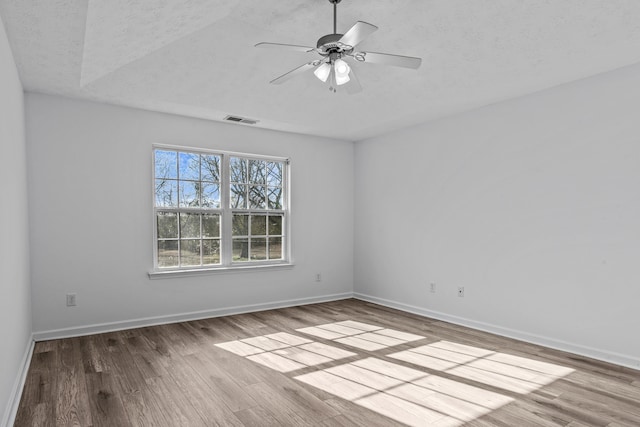 spare room with visible vents, a ceiling fan, a textured ceiling, wood finished floors, and baseboards