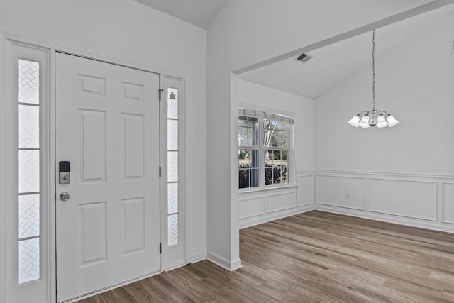 foyer with wood finished floors, visible vents, vaulted ceiling, wainscoting, and an inviting chandelier